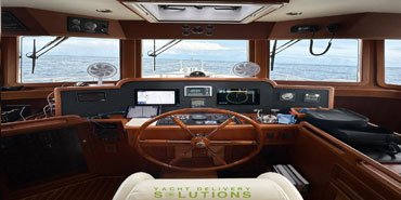 The image shows the interior of a boat's control room. The room is well-lit and has a modern feel, with a large window offering a view of the sea. The control panel is equipped with various gauges, screens, and buttons, suggesting a high-tech and advanced system. There are two chairs facing the control panel, indicating that it's a place for two people to operate the boat. The overall impression is one of a comfortable and functional space designed for navigating the waters.