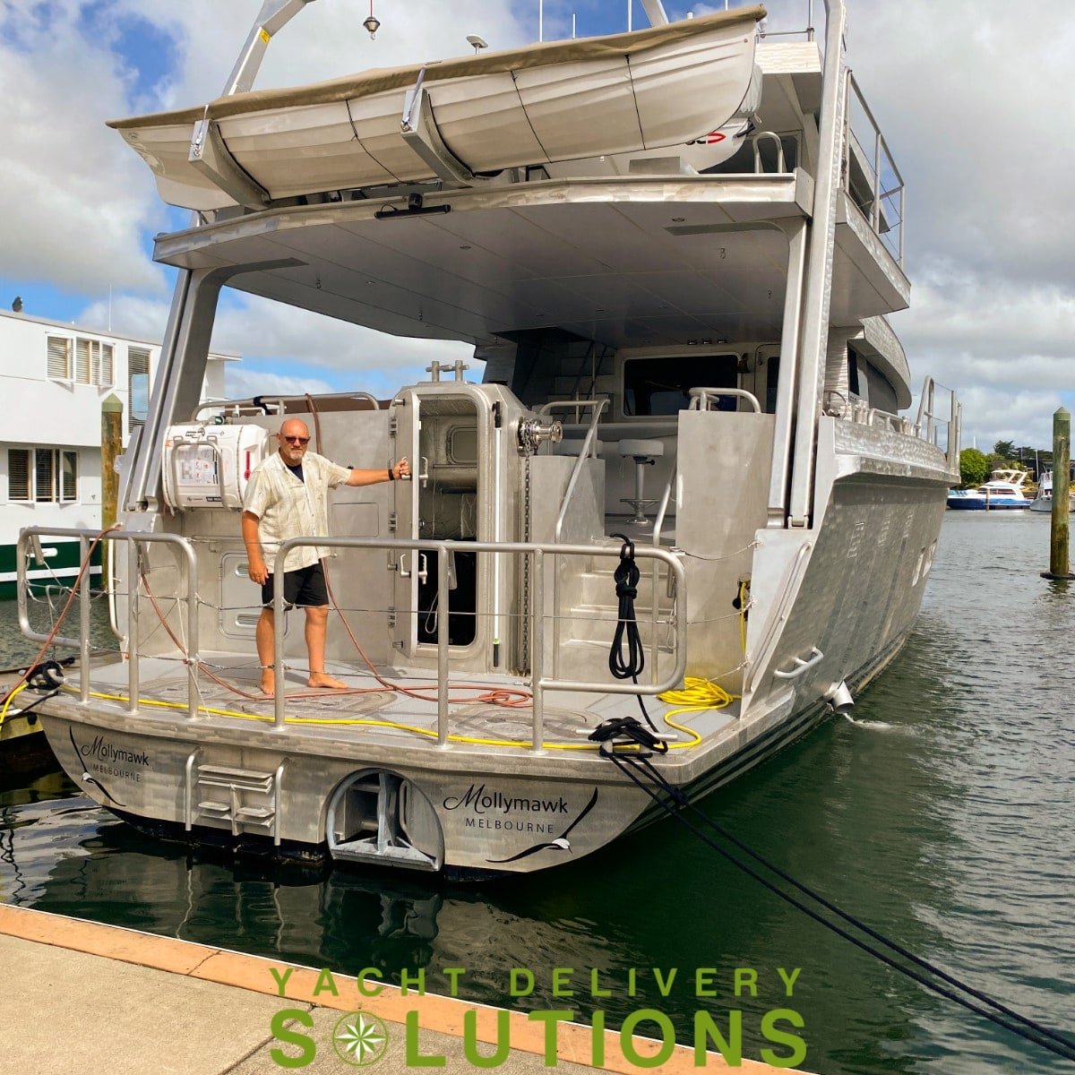 Circa 25 meter power Boat shown from the stern with the delivery Skipper standing on the aft section. the vessel is dark grey and spectacular